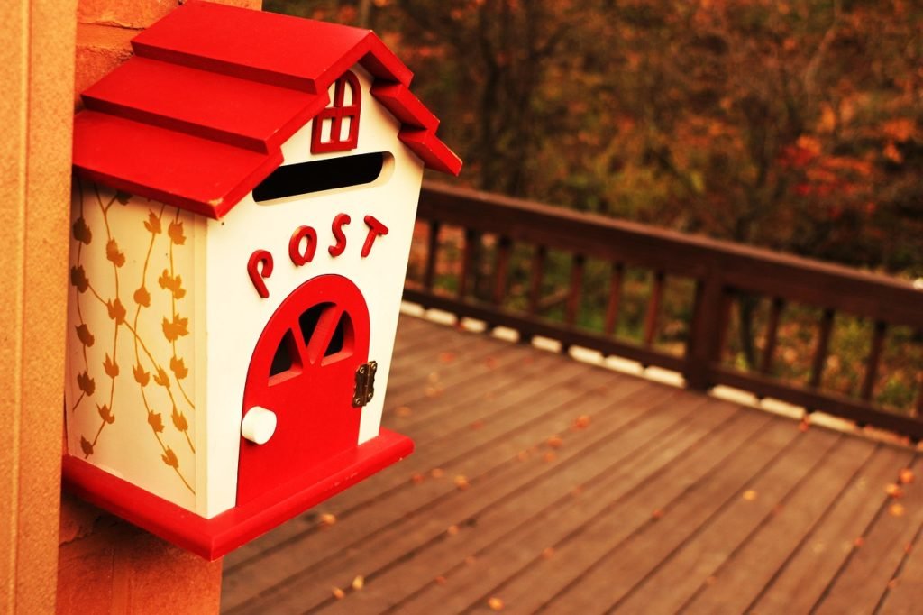 a cute wall-mounted mailbox shaped like a house with a red roof and front door