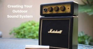 a small guitar amplifier sitting on a glass-top patio table, with a garden wall and some greenery in the back. Text reads, creating your outdoor sound system